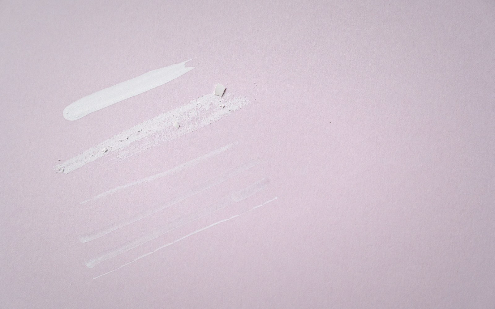 White cream and powder swatches smeared in lines on a pale pink surface
