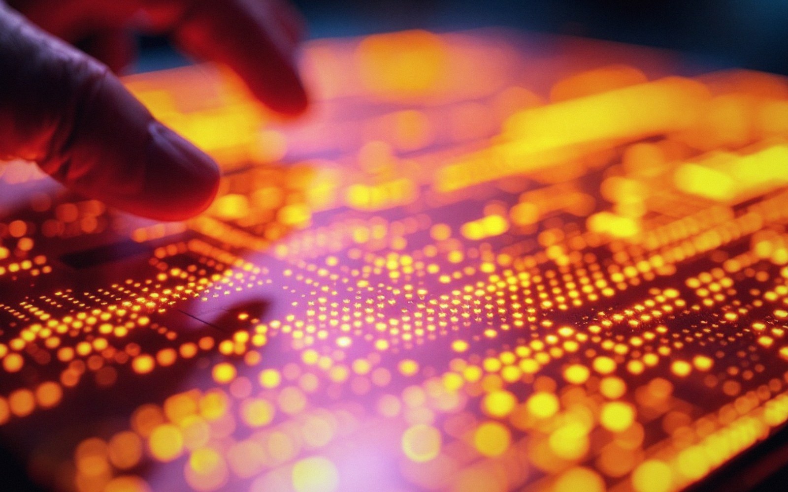 A finger touches a glowing circuit board covered in orange and yellow illuminated dots